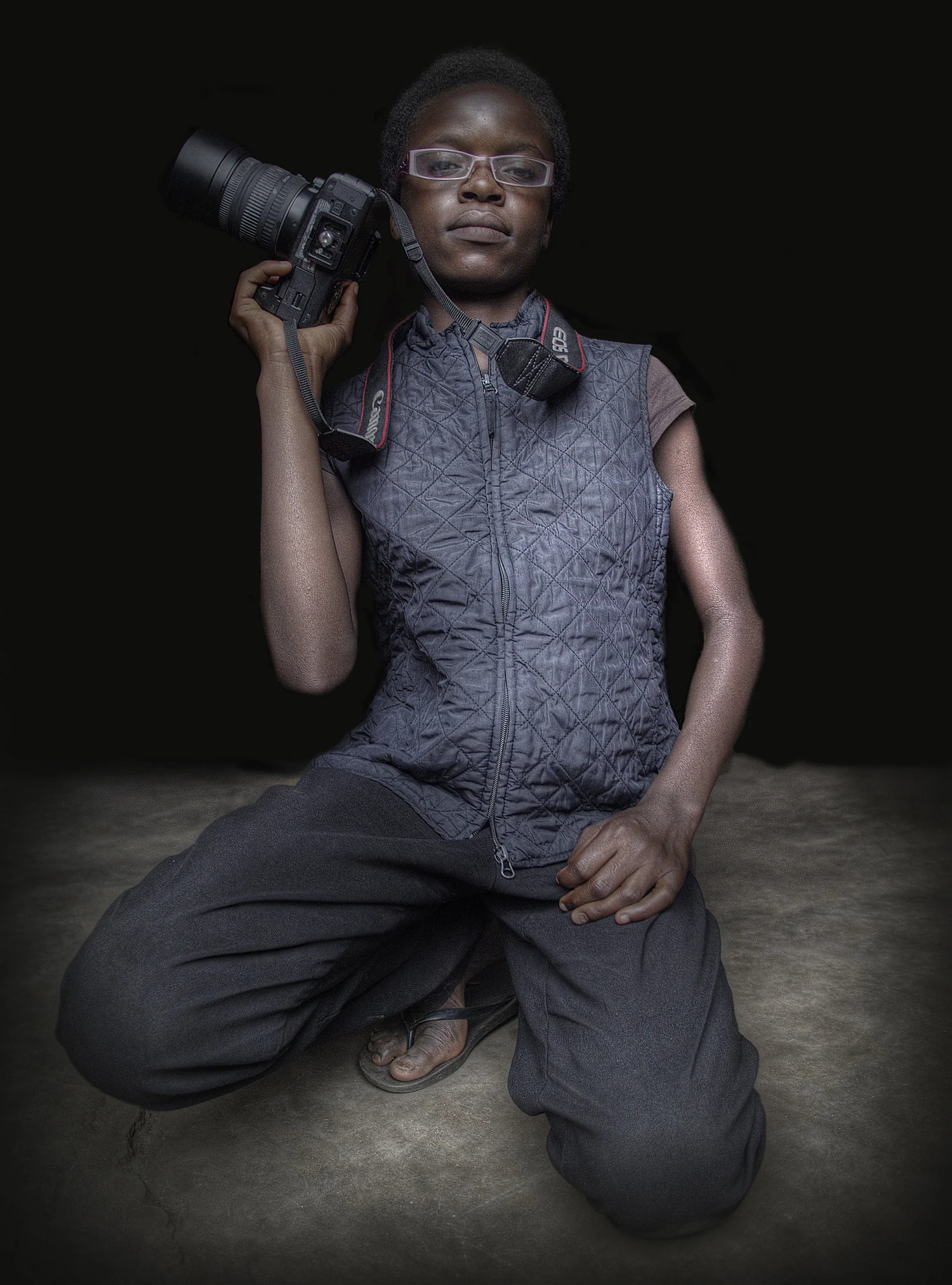 Portrait of a young photographer kneeling in a studio, holding a camera to their eye