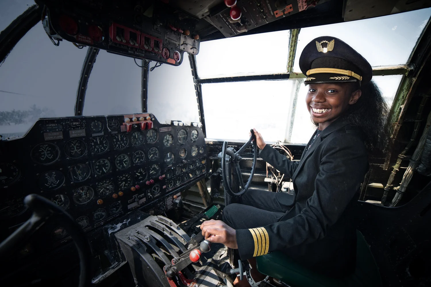 Woman in a pilot uniform smiling from the controls of an aircraft cockpit