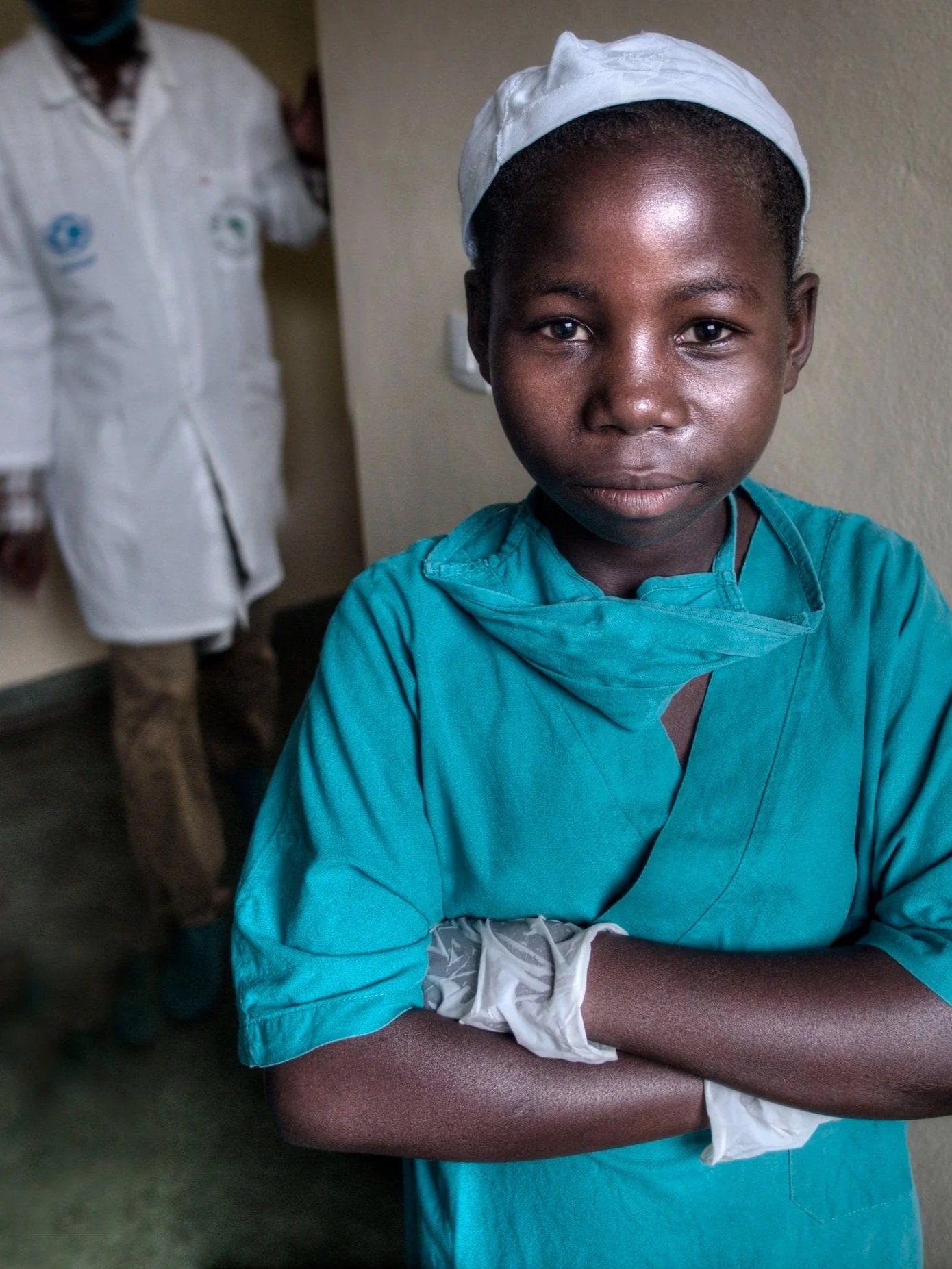 Girl in surgical scrubs standing with arms crossed in front of adult doctors